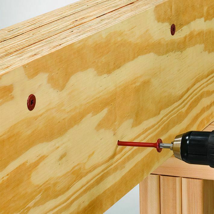 This image depicts a hand drill drilling a red screw into a piece of plywood.